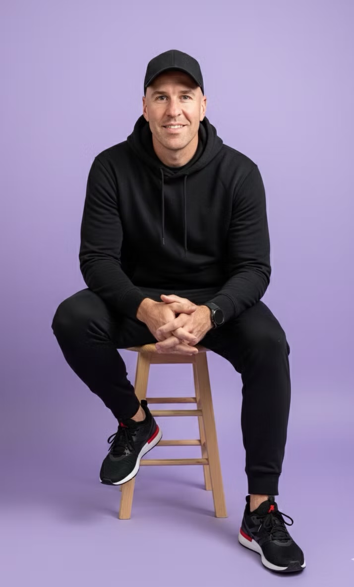 Portrait of DJ Jake seated on a stool, wearing a black hoodie and cap